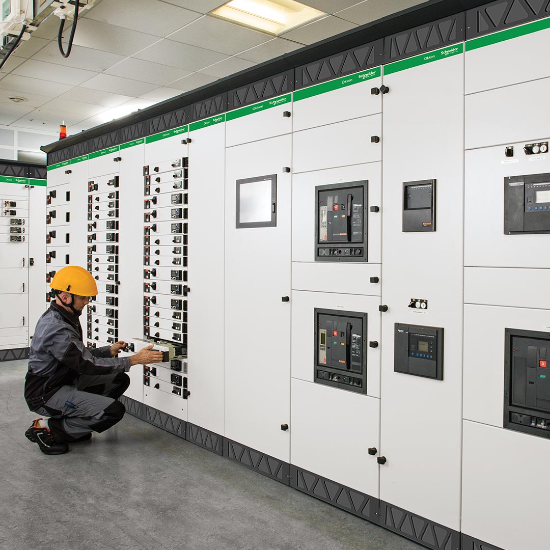 A Schneider Electric technician working on an Okken low-voltage switchboard cabinet.